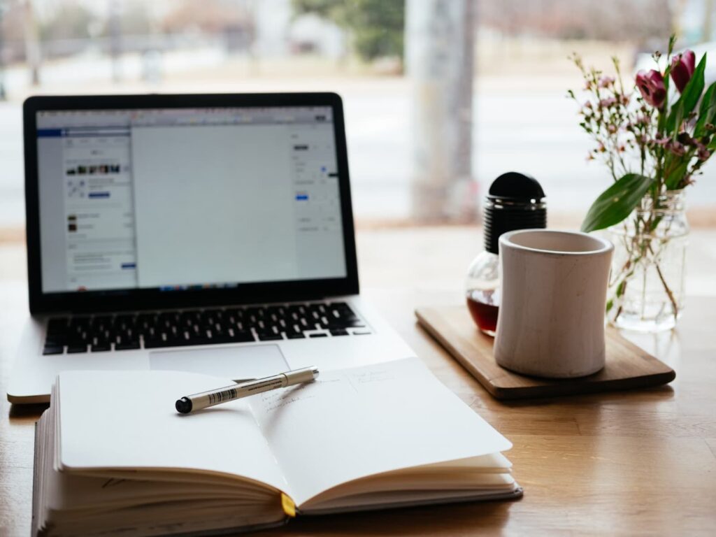 MacBook with a coffee mug and a notepad on a wooden table.