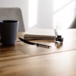 A serene workspace with a mug, notebook, and pen on a wooden table.